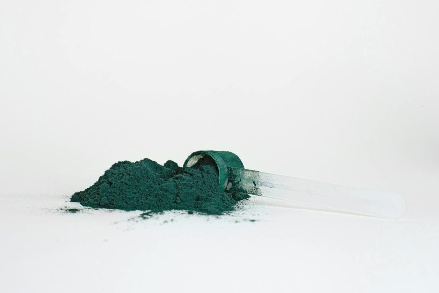 A pile of spirulina powder in a transparent measuring scoop isolated on a white background.