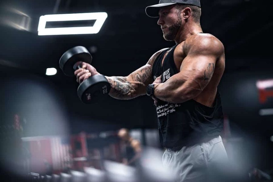 A muscular man in sportswear lifting dumbbells indoors, showcasing strength and fitness.