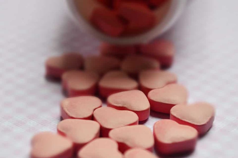 Close-up of heart-shaped pink pills spilled from a bottle on a soft surface.