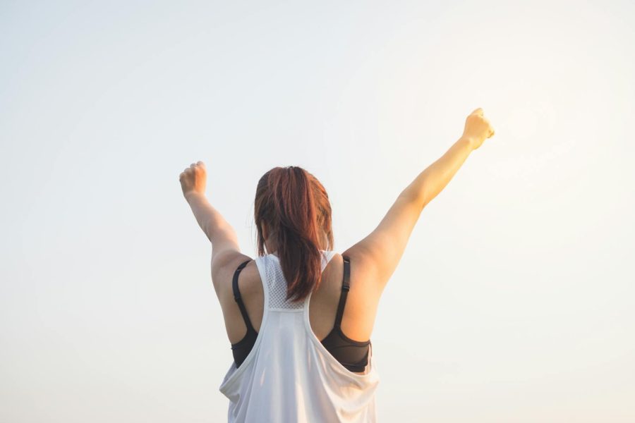 A woman celebrates success with arms raised in a bright outdoor setting.