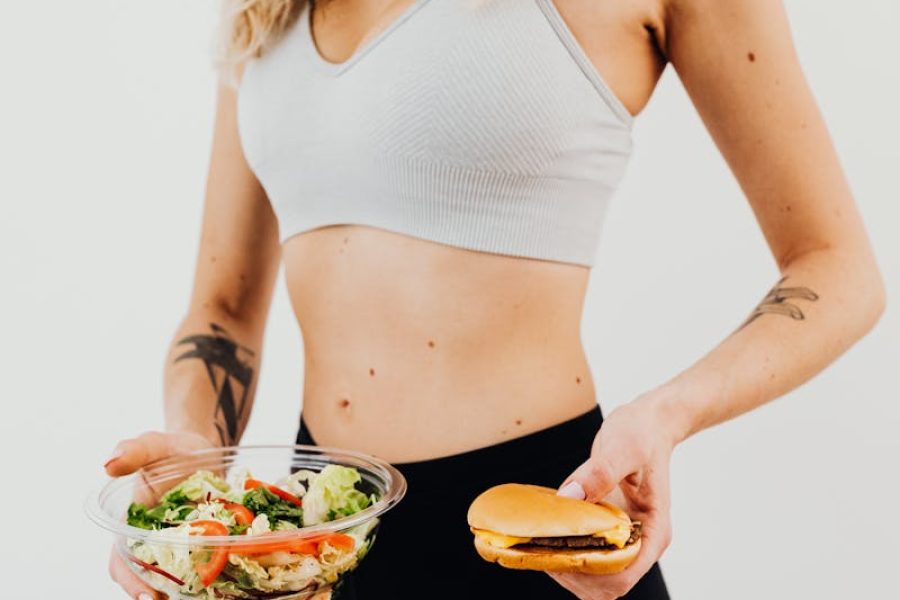 Smiling woman in sportswear balances healthy salad vs junk food choice.