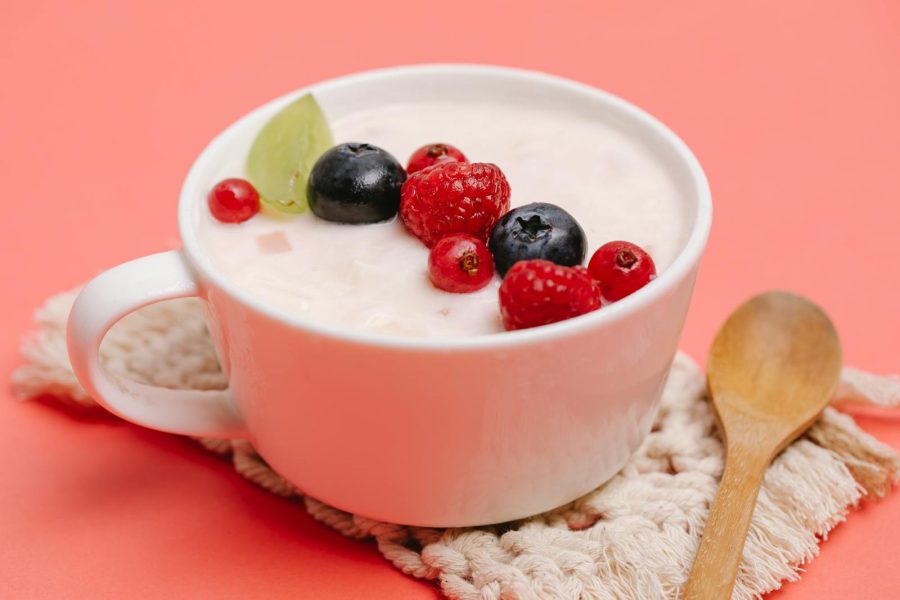 Top view of a white cup filled with yogurt and assorted berries on a pink background.