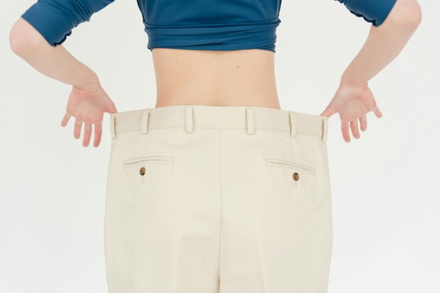 A woman's back view showcasing weight loss with oversized pants in a studio setting.