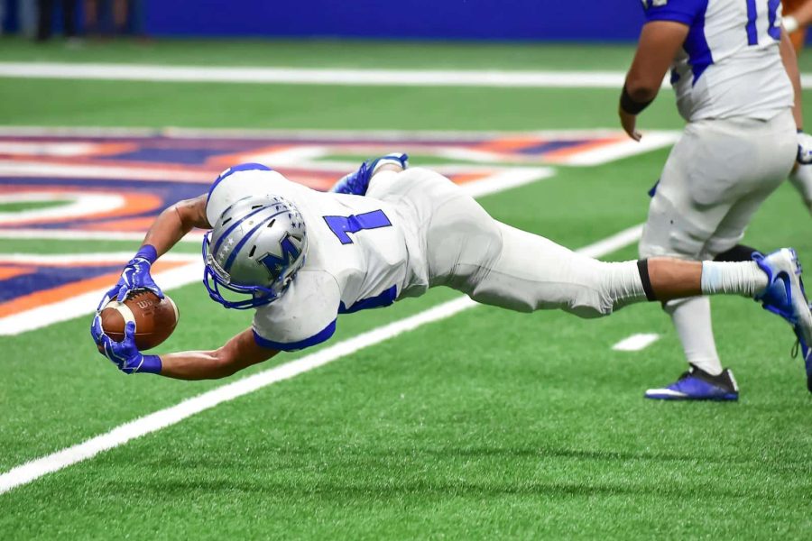 Football player making an incredible diving catch during a high-energy game in the stadium.