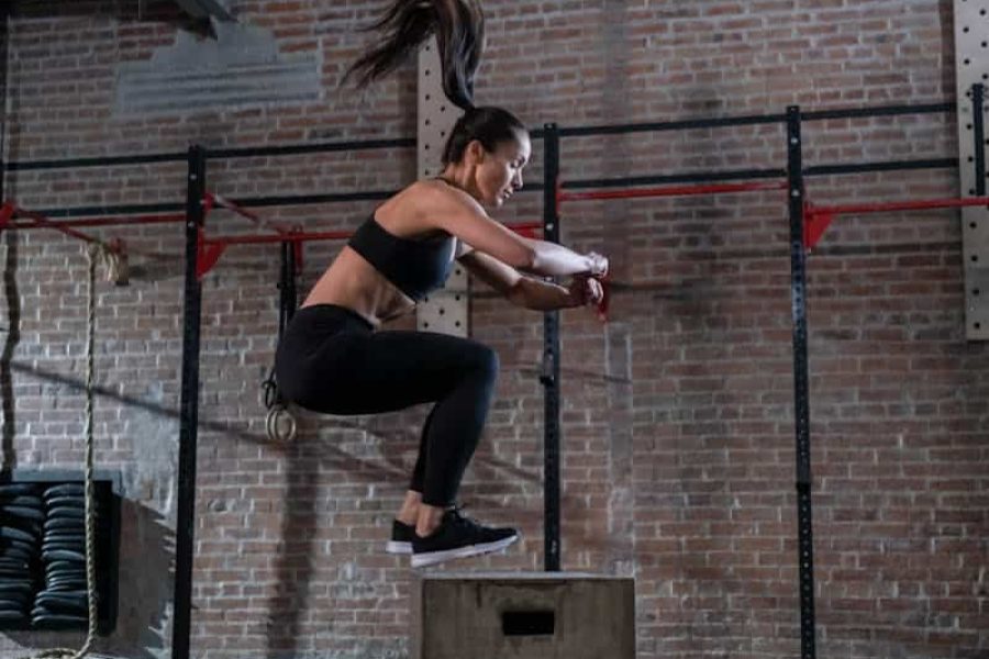 A fit woman executes a box jump in a gym setting, showcasing athleticism and fitness.