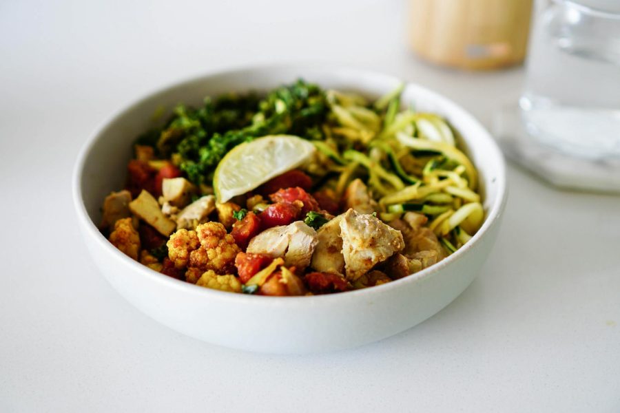 A nutritious bowl containing zoodles, roasted cauliflower, chicken, and a lemon slice, perfect for healthy eating.